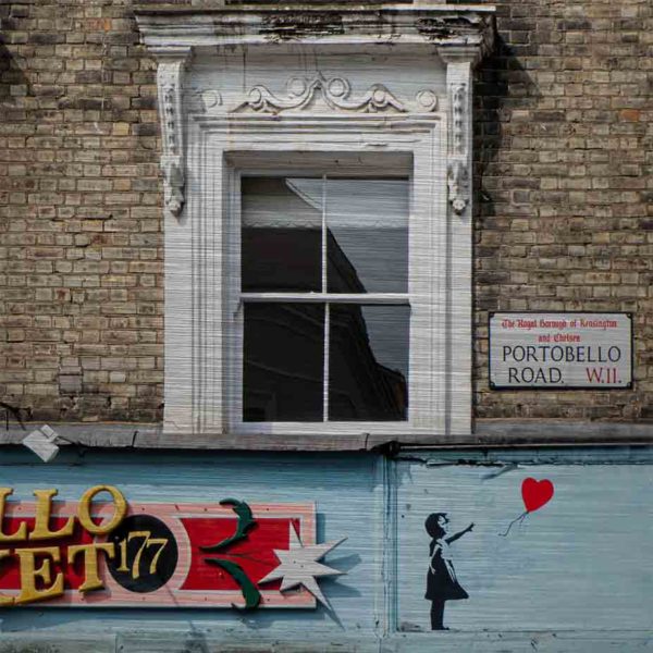 London Streetart Graffiti. Es zeigt das Bild einer Hausfront mit 3 Fenstern. An der Backsteinwand ist ein Straßenschild mit der Straßenbezeichnung „Portobello Road“. Unter den Fenstern ist der Schriftzug eines Geschäftes mit dem Namen „Portobello Market“ und an der rechten Seite des Schildes ist die Figur eines Mädchens abgebildet, welches einen Luftballon in Herzform gerade losgelassen hat. Die Fenster sind Weiß, die Backsteinwand hellgrau und Schild des Geschäftes ist in den Farben, Hellblau, Rot, Rose, Schwarz und Gold.