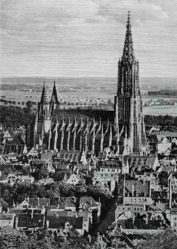 Das Bild zeigt eine komplette Seitenansicht des Ulmer Münsters aus größerer Entfernung. Das historische Bild aus weiterer Entfernung zeigt die komplette Kirche mit seinen Türmen umringt von den Häusern der Stadt. Das Bild ist in den Farben Schwarz-Weiss.