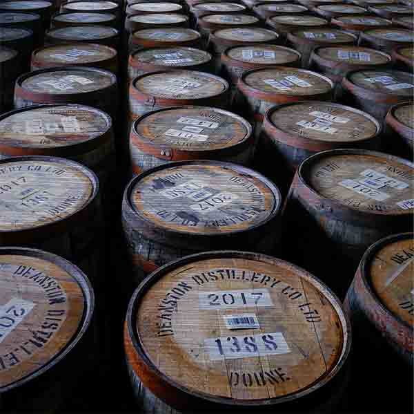 Schottland Brennerei Deanston Whiskyfässer. Es zeigt das Bild von Whiskyfässern in einer Destillerie in den schottischen Highlands. Die Holzfässer sind stehend mit dem Fassdeckel nach oben, so dass die Bezeichnung der Inhalte gut zu lesen ist. Das Bild ist quadratisch und in Farbe.