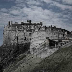 Schottland Edinburgh. Es zeigt das Bild des Wahrzeichens der Stadt Edinburgh, die Höhenburg „Edinburgh Castle“, gelegen auf einem Felsen dem „Castle Rock“. Die Burg ist aus grauem Naturstein und es sind 2 Gebäude der Burg zu sehen. Ein Gebäude ist rund und das andere Gebäude ist eckig. Unter dem eckigen Gebäude ist der Felsen zu sehen auf dem die Burg gebaut ist. Außerdem ist eine Mauer zu sehen, hinter welcher sich der Vorhof zur Burg befindet. Das Bild ist im Querformat und in Farbe.
