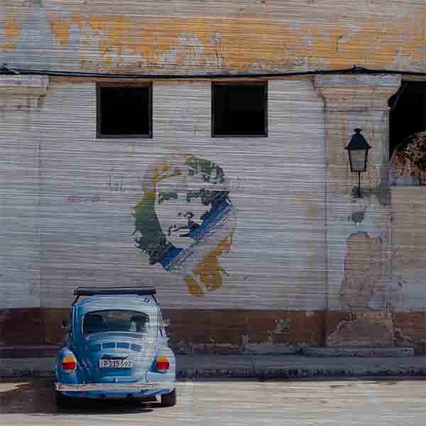 Havanna Che Guevara. Es zeigt das Bild eines VW Käfers welcher vor einem Graffiti des kubanischen Revolutionskämpfers Che Guevara geparkt ist. Das Graffiti ist auf ein leicht verfallenes typisches kubanisches Gebäude gesprüht. Der VW-Käfer hat die Farbe Blau und das Graffiti von Che Guevara ist in den Farben Blau, Grün, Gelb und Weiß. Das Gebäude hat oben 2 größere Fenster und darunter 2 kleinere Fenster. An dem Gebäude ist eine kleine Laterne angebracht. Das Alu Dibond Bild ist quadratisch